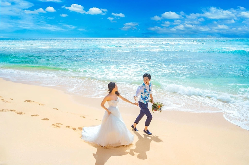 白浜を走るウエディングドレス姿の新婚カップル