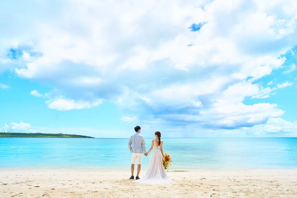 透き通る青い海と広い空を眺めながら手をつないで立つ新郎新婦の後ろ姿