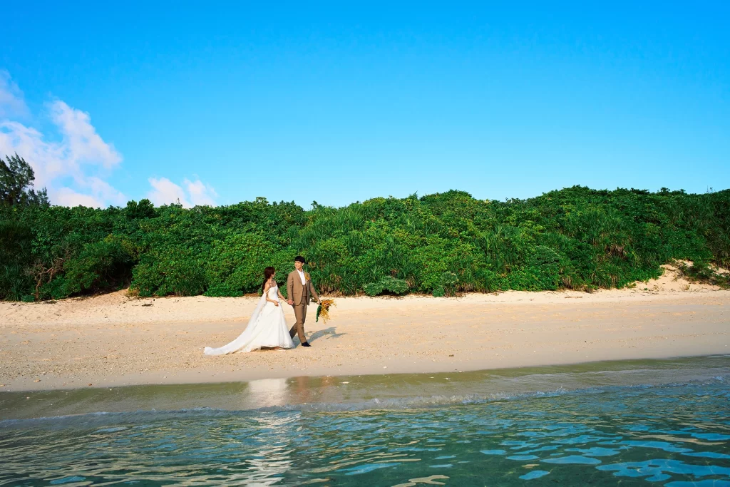 青空の下、宮古島の砂浜を寄り添って歩く新郎新婦