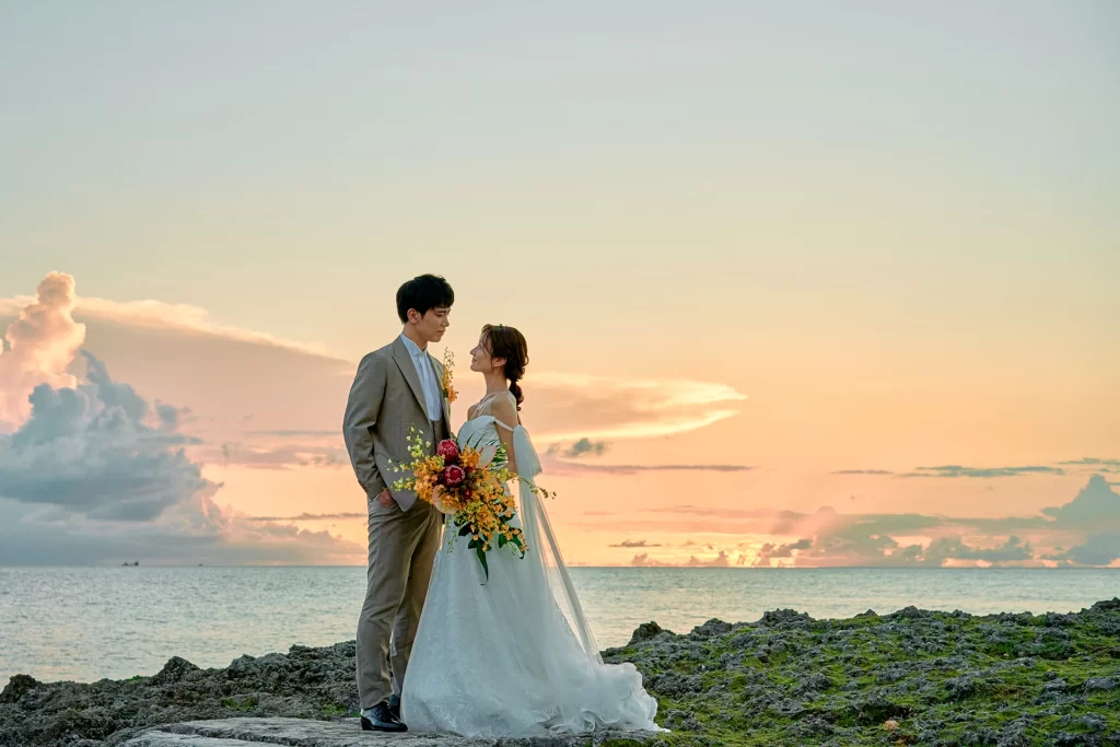 夕焼け空と海を背景に寄り添って立つ新郎新婦のドラマチックなウェディングフォト