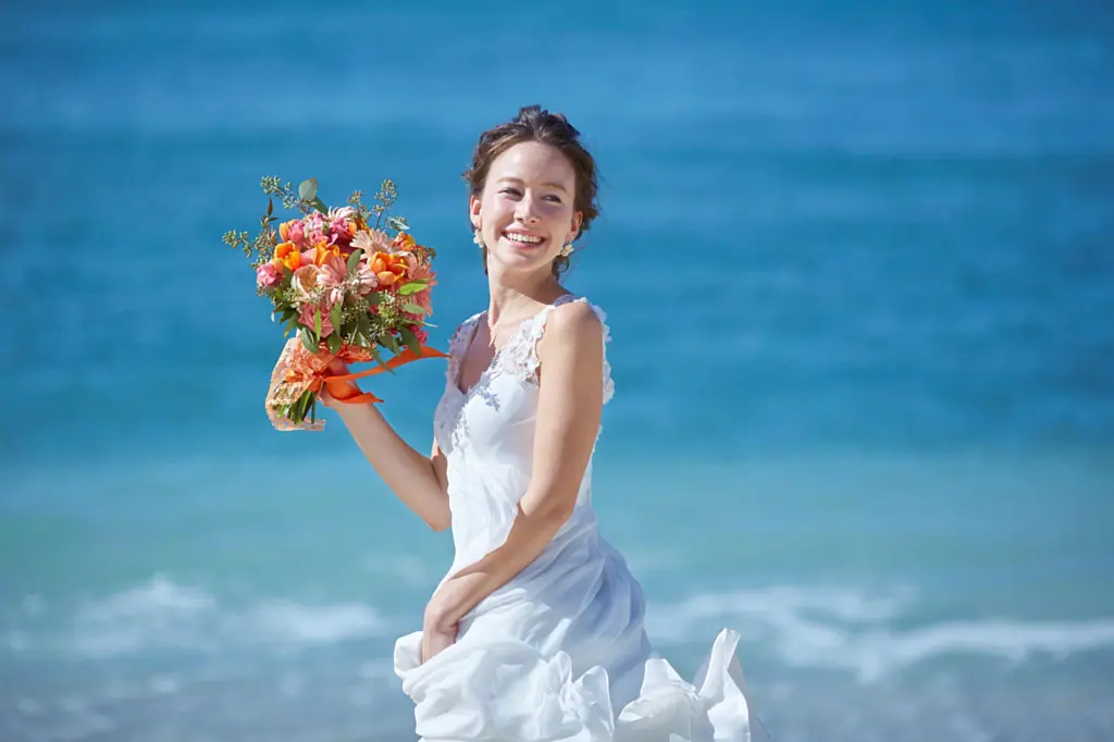 青い海を背景にブーケを手に微笑む海外リゾート挙式の花嫁