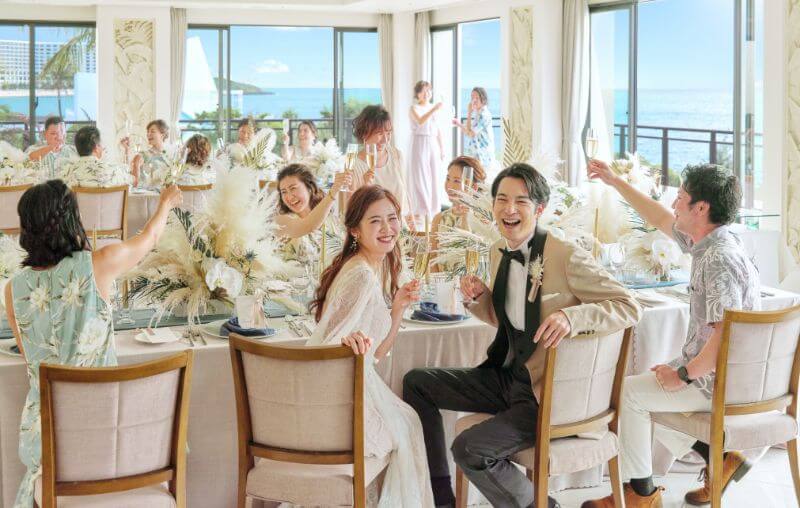 写真:結婚披露パーティで参列者とともに満面の笑顔で乾杯する新郎新婦