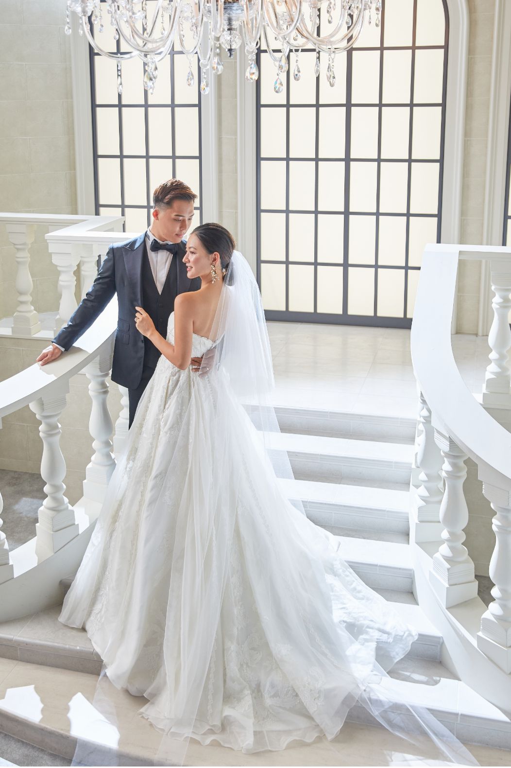 白亜のゲストハウスの階段に座りポーズを決めるタキシードとウェディングドレス姿の新郎新婦の写真
